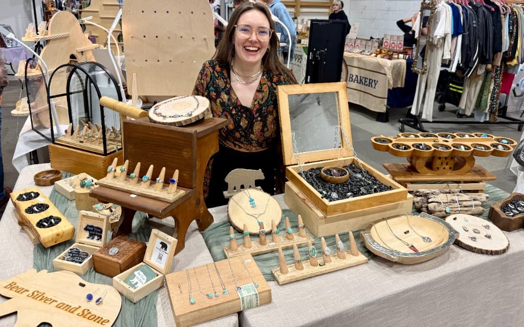 Claire at the Bear Silver & Stone booth — silver and turquoise jewelry on wooden displays at an indoor market